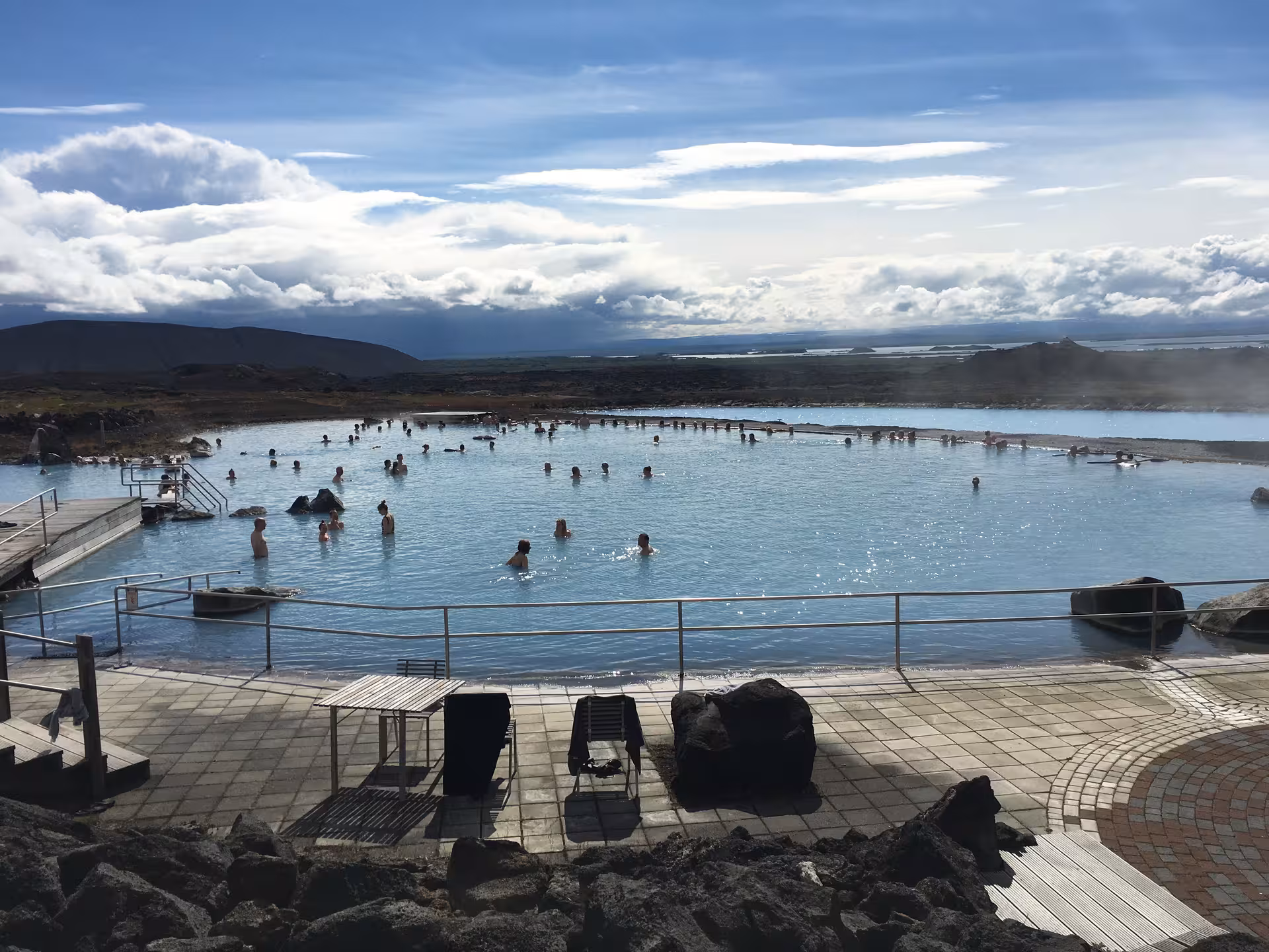 Visitors enjoy a relaxing soak in the tranquil geothermal waters of the Myvatn Nature Baths under a bright sky.
