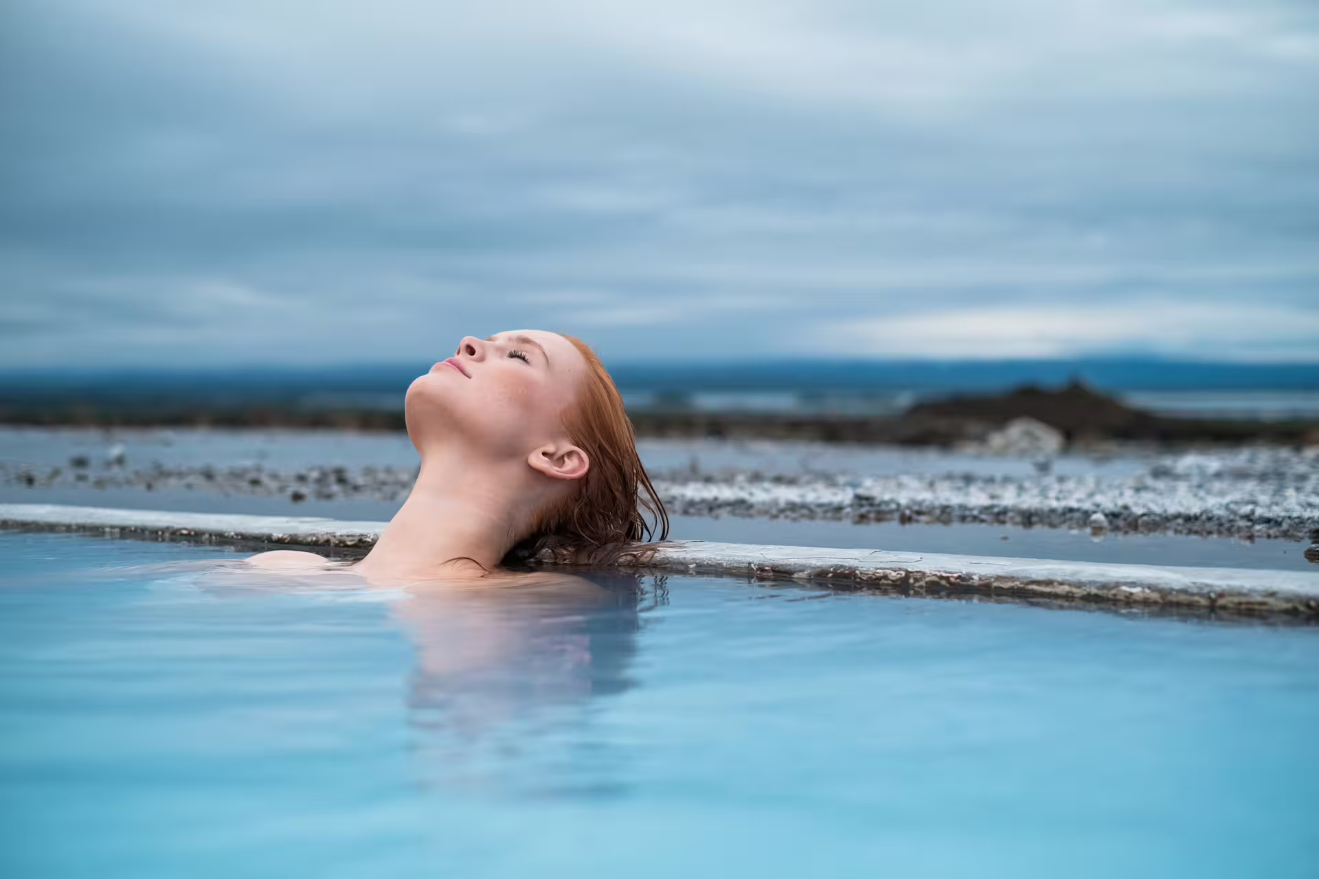 Woman relaxing in Myvatn Nature Baths geothermal pool with cloudy sky backdrop