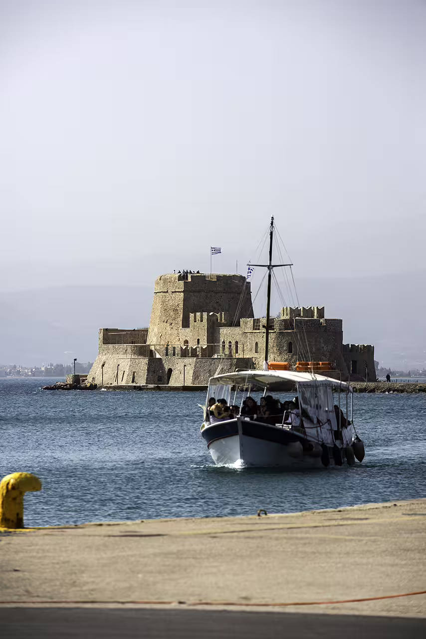 Tour boat approaching Nafplion waterfront with Bourtzi Fortress behind, on an Ancient Corinth and Nafplion full-day trip