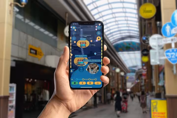Hand holding smartphone displaying Nagasaki self-guided walking tour app in a covered shopping arcade