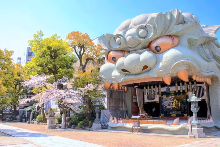 Giant lion-head shrine entrance at Namba Yasaka Jinja with cherry blossoms in Osaka