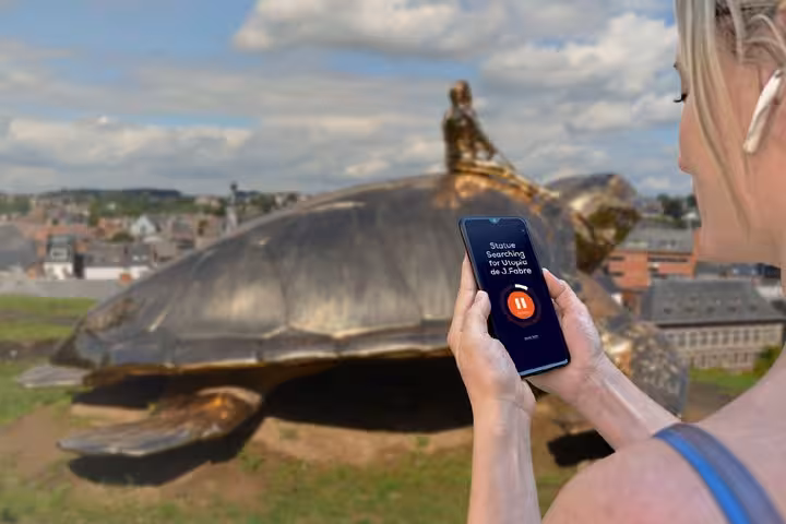 Tourist using audio guide app on smartphone with giant turtle statue in Namur, Belgium