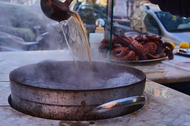 Steaming broth being poured into a pot with fresh octopus in the background on a Naples street.