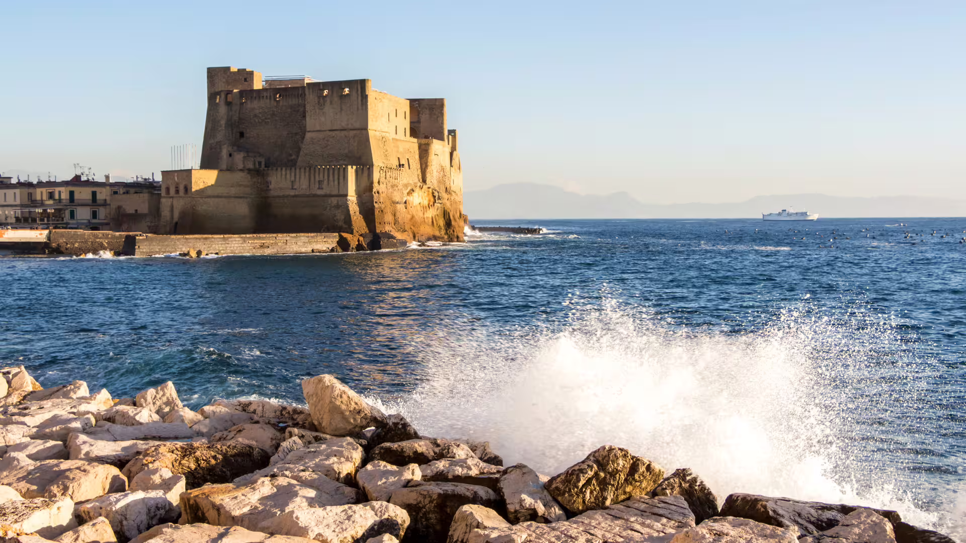 Vista sul Castel dell’Ovo e sul lungomare di Napoli con onde che si infrangono, tappa panoramica del tour guidato
