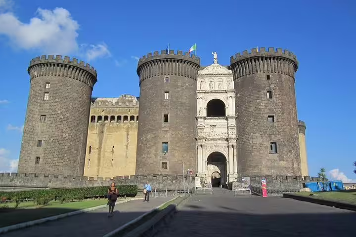 Guided Naples city tour stop at medieval Castel Nuovo Maschio Angioino fortress with imposing towers under a clear blue sky
