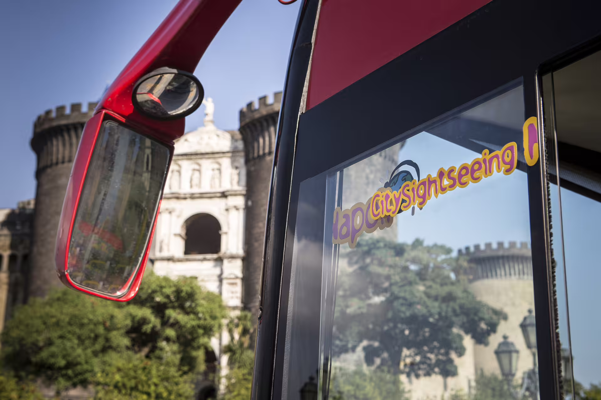 Close-up of Naples hop on hop off sightseeing bus with Castel Nuovo Maschio Angioino in background on sunny day