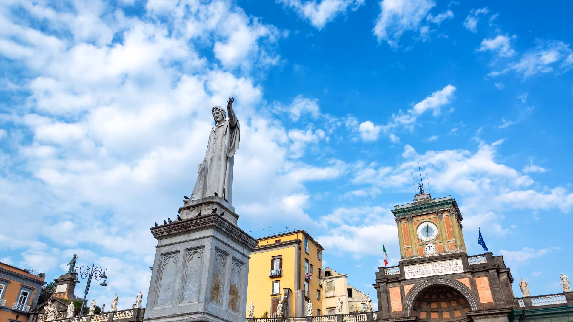 Statue and historic architecture under a bright sky in Naples, featured in the Italian folklore tour.