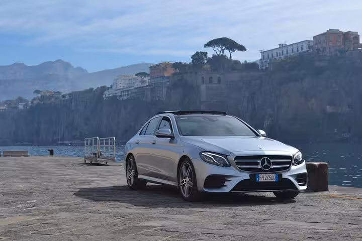 Sleek silver Mercedes sedan on coastal road with scenic cliffside backdrop, ready for Naples to Positano transfer.