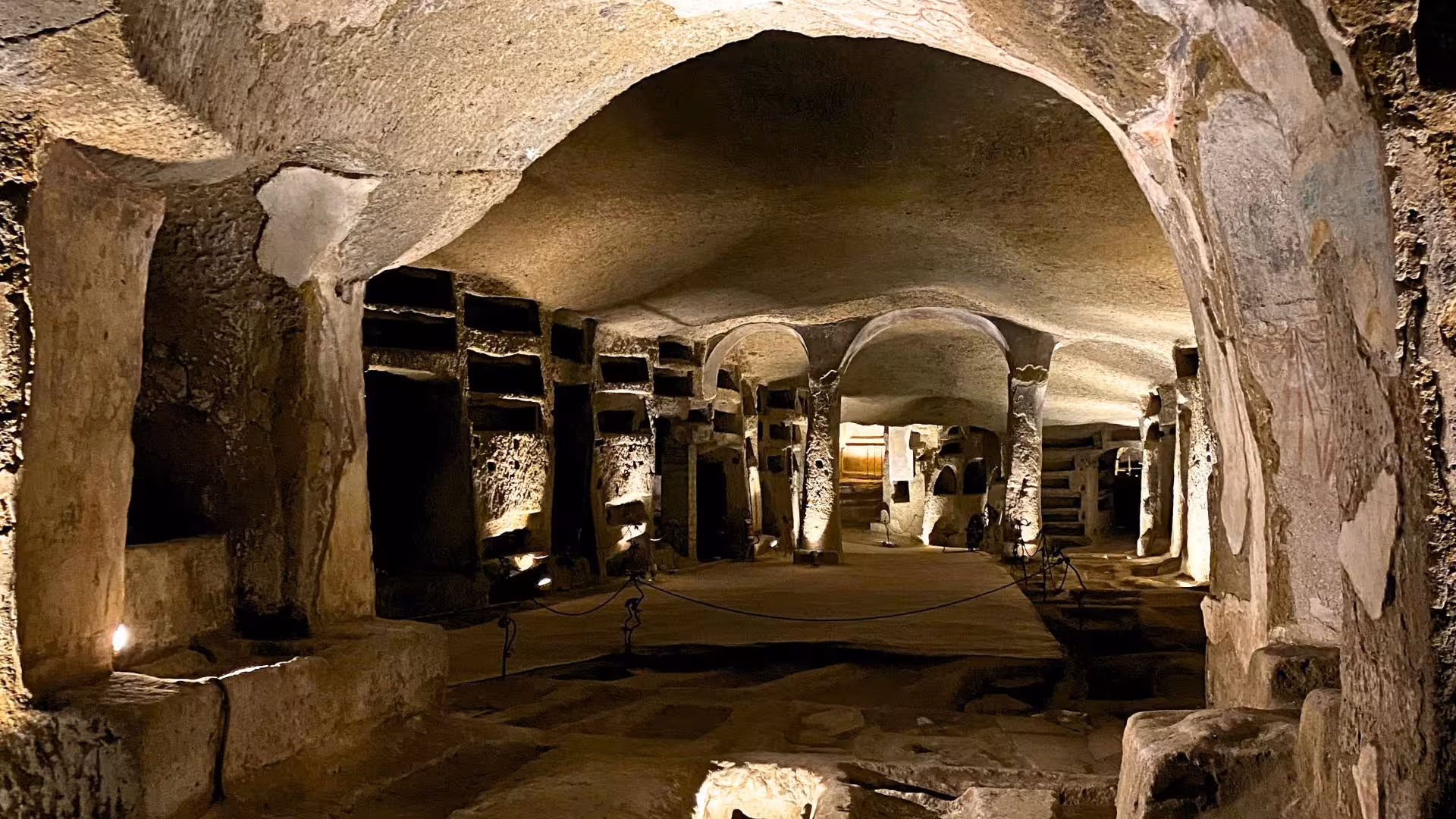 Discover the ancient catacombs of Naples' Sanità district, showcasing historical burial sites and stone arches.