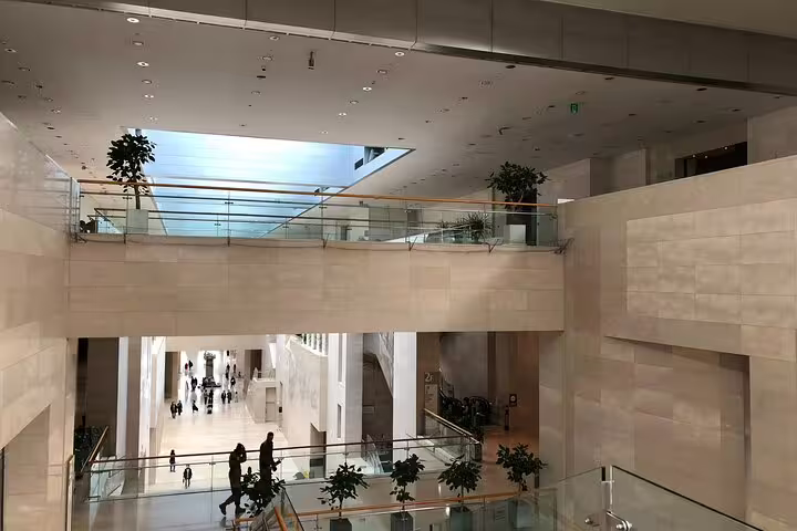 Multi-level atrium interior of National Museum of Korea with glass railings, plants, and visitors walking below