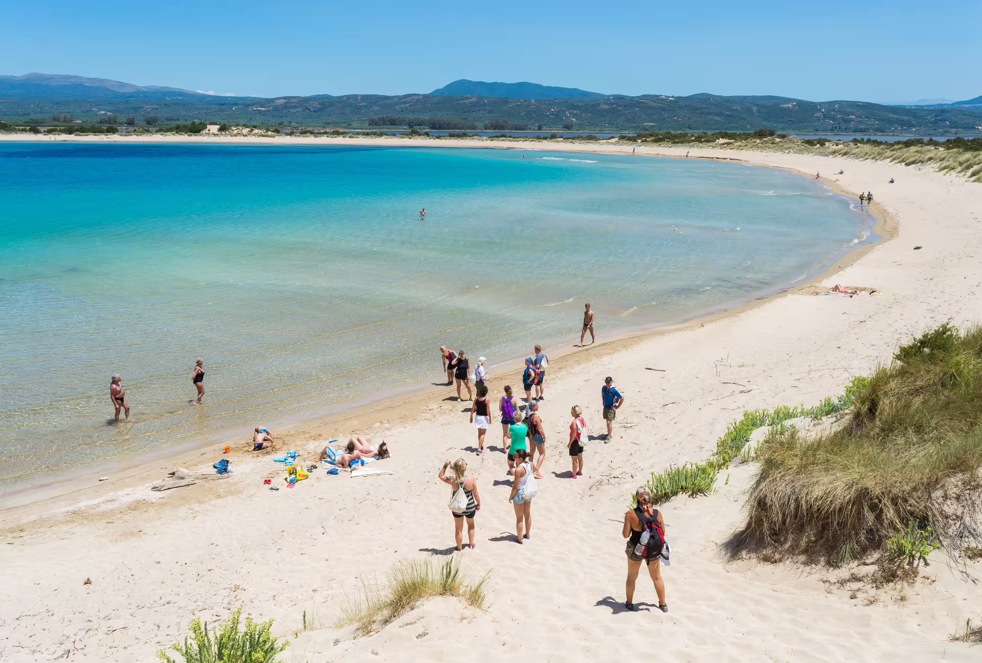 Hikers and beachgoers on golden dunes and shallow turquoise lagoon during Navarino Bay hiking tour, Pylos