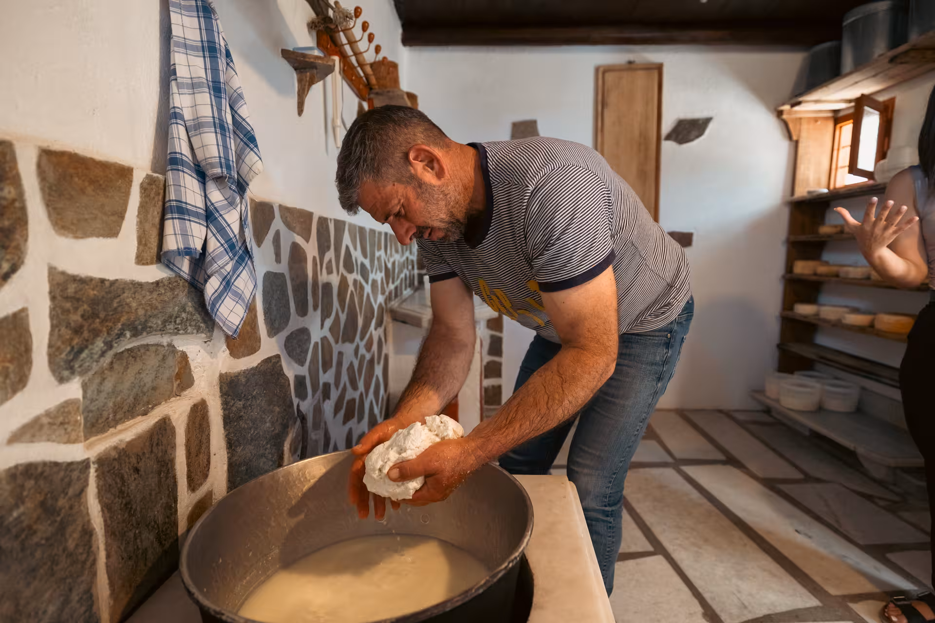 Cheesemaker shaping curds in a vat during Naxos traditional cheesemaking class inside an authentic island dairy