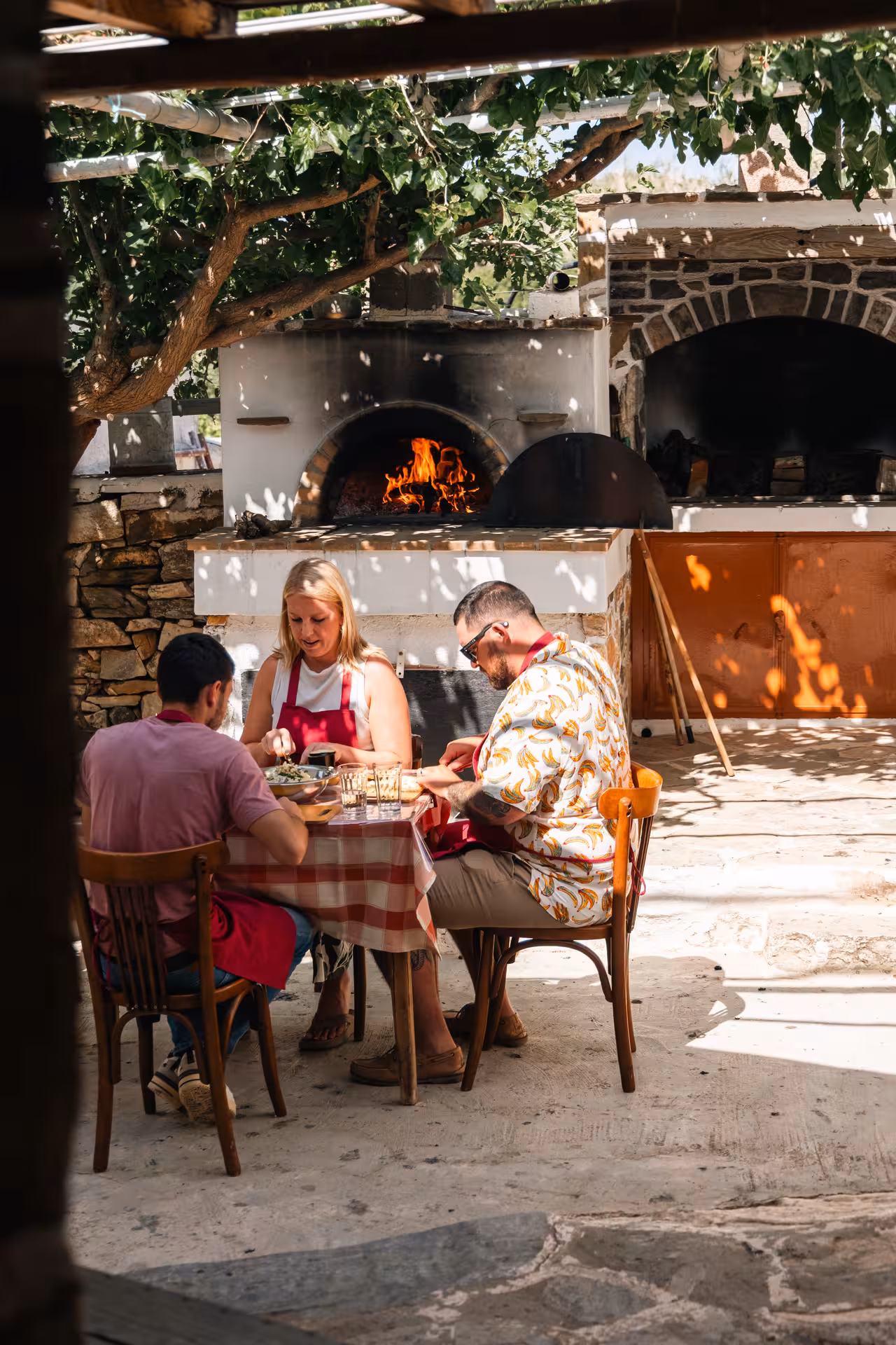 Guests dine after Naxos traditional cooking and cheesemaking class beside a wood-fired oven in a village courtyard