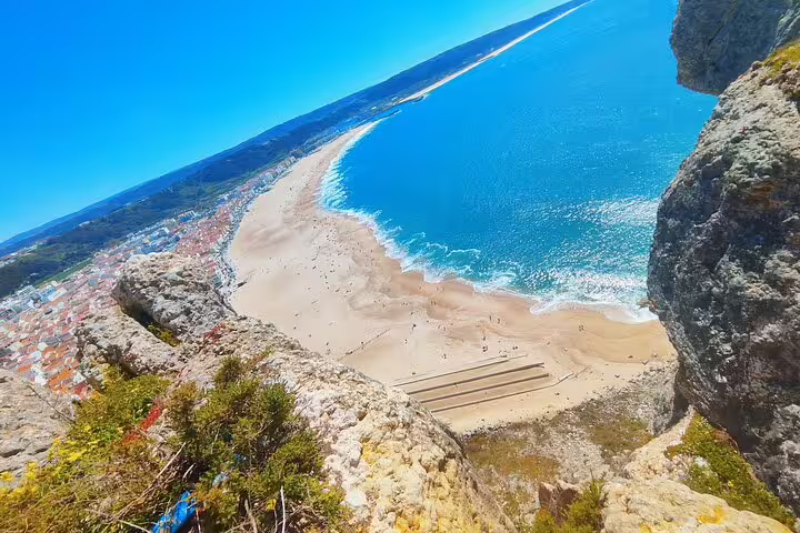 Aerial view of Nazaré’s stunning crescent beach, surrounded by rocky cliffs and vibrant ocean waves.