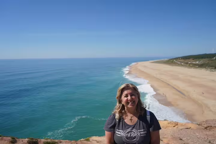 Woman smiling on a cliff overlooking the stunning beach of Nazaré, a highlight of the full-day private tour from Lisbon.