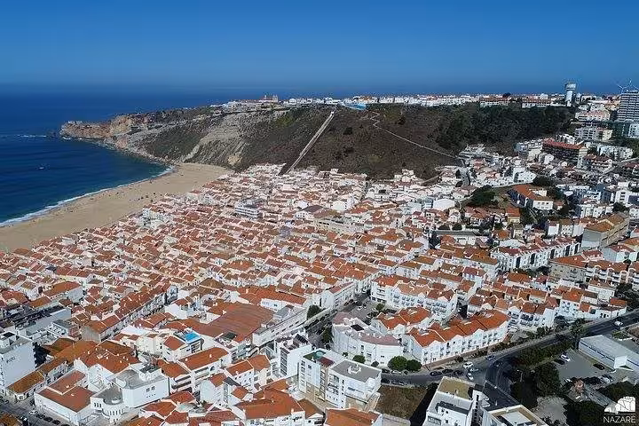 Aerial view of Nazare beach and cliffside town, a highlight on Coimbra Nazare Obidos day trip Portugal