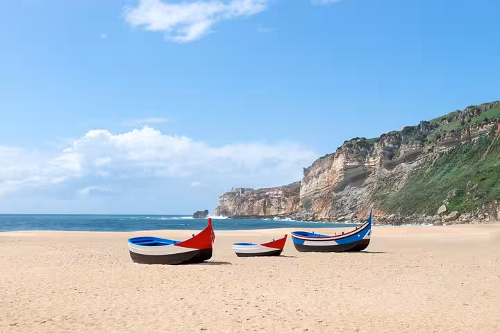 Nazaré beach with colorful fishing boats and scenic cliffs under a clear blue sky, ideal for a coastal Portugal tour.