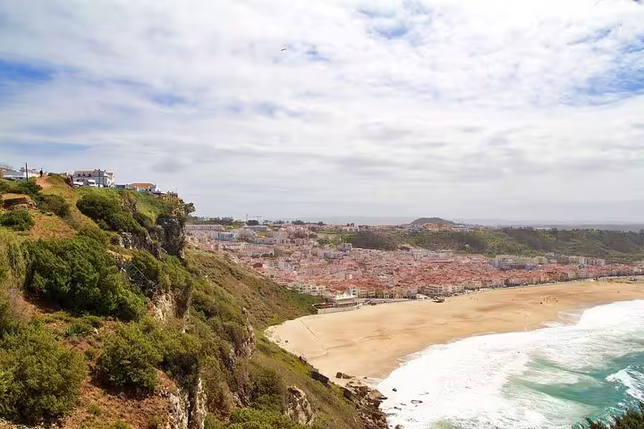Scenic view of Nazaré's sandy beach and coastal town from a lush cliff, ideal stop on Lisbon to Porto transfer.