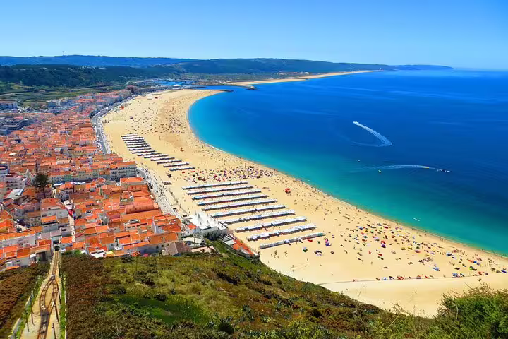 Aerial view of Nazaré beach with vibrant umbrellas and calm blue waters, ideal for a coastal stop on the Portugal tour.