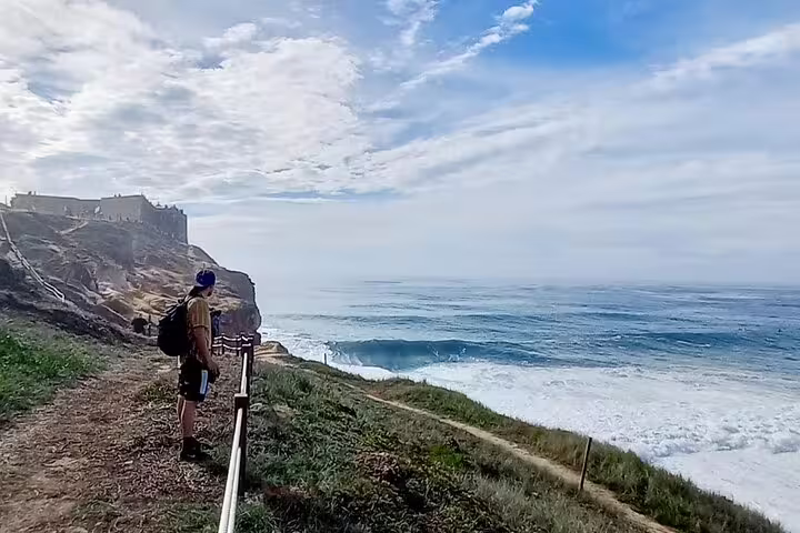 A traveler overlooks the cliffs and ocean waves at Nazaré, a scenic stop on the Fatima-Nazare-Obidos private tour.
