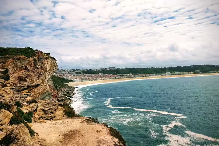 Scenic coastal view of Nazaré with cliffs and ocean waves, featured on a Lisbon small group tour to Fátima, Nazaré, and Óbidos.