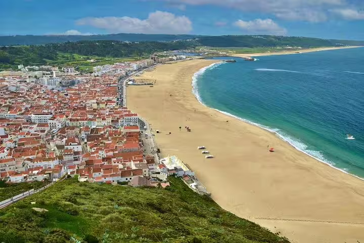 Aerial view of Nazare's stunning coastline with sandy beaches and vibrant town, featured in a full-day tour from Lisbon.