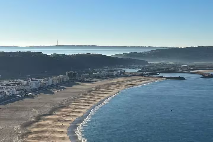 Aerial view of Nazaré's stunning coastline with sandy beaches and calm blue waters, featured in the Fátima, Nazaré, and Óbidos tour.