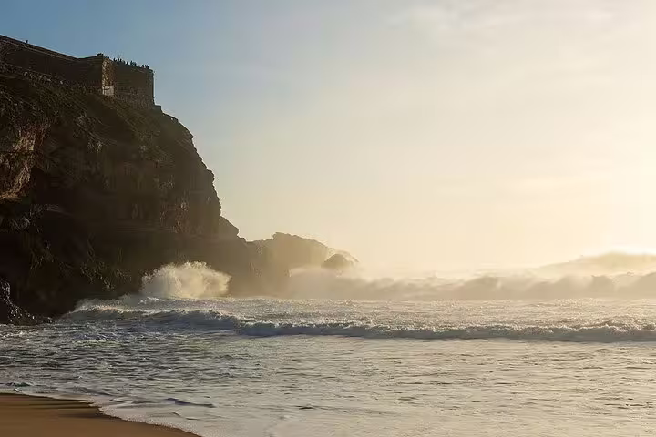 Sunset view of Nazaré's dramatic coastline with waves crashing against the cliffs, perfect for the Fátima, Nazaré, and Óbidos tour.