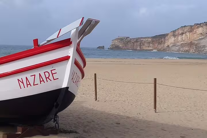 Traditional fishing boat on Nazaré beach with scenic cliffs, featured in Fatima-Nazare-Obidos private tour.