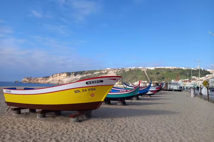 Colorful fishing boats on Nazaré beach under a blue sky, part of Fatima-Nazare-Obidos private tour experience.