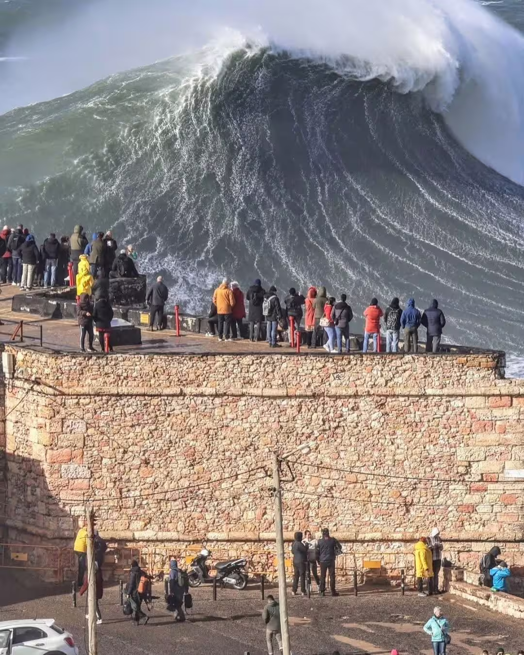 Spectators watch massive waves at Nazaré, Portugal, famous for its giant surf, ideal for extreme surfing adventures.