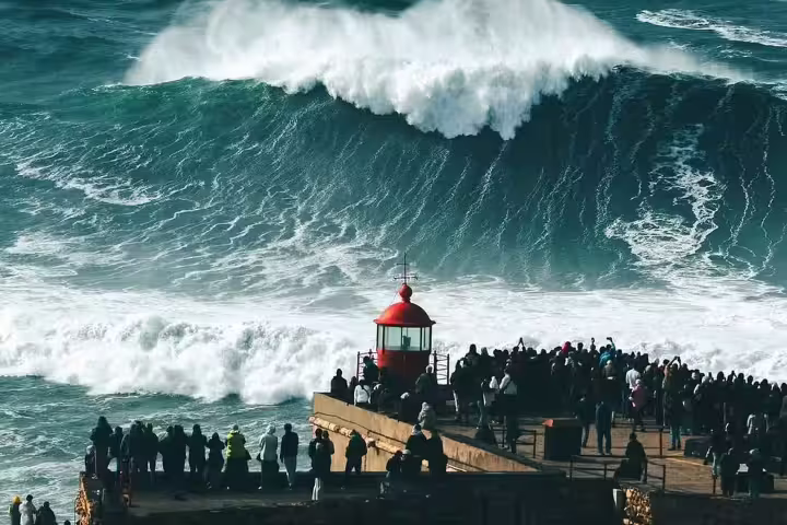 Spectators gather at Nazaré's iconic lighthouse to witness the breathtaking giant waves, a must-see surf experience in Portugal.