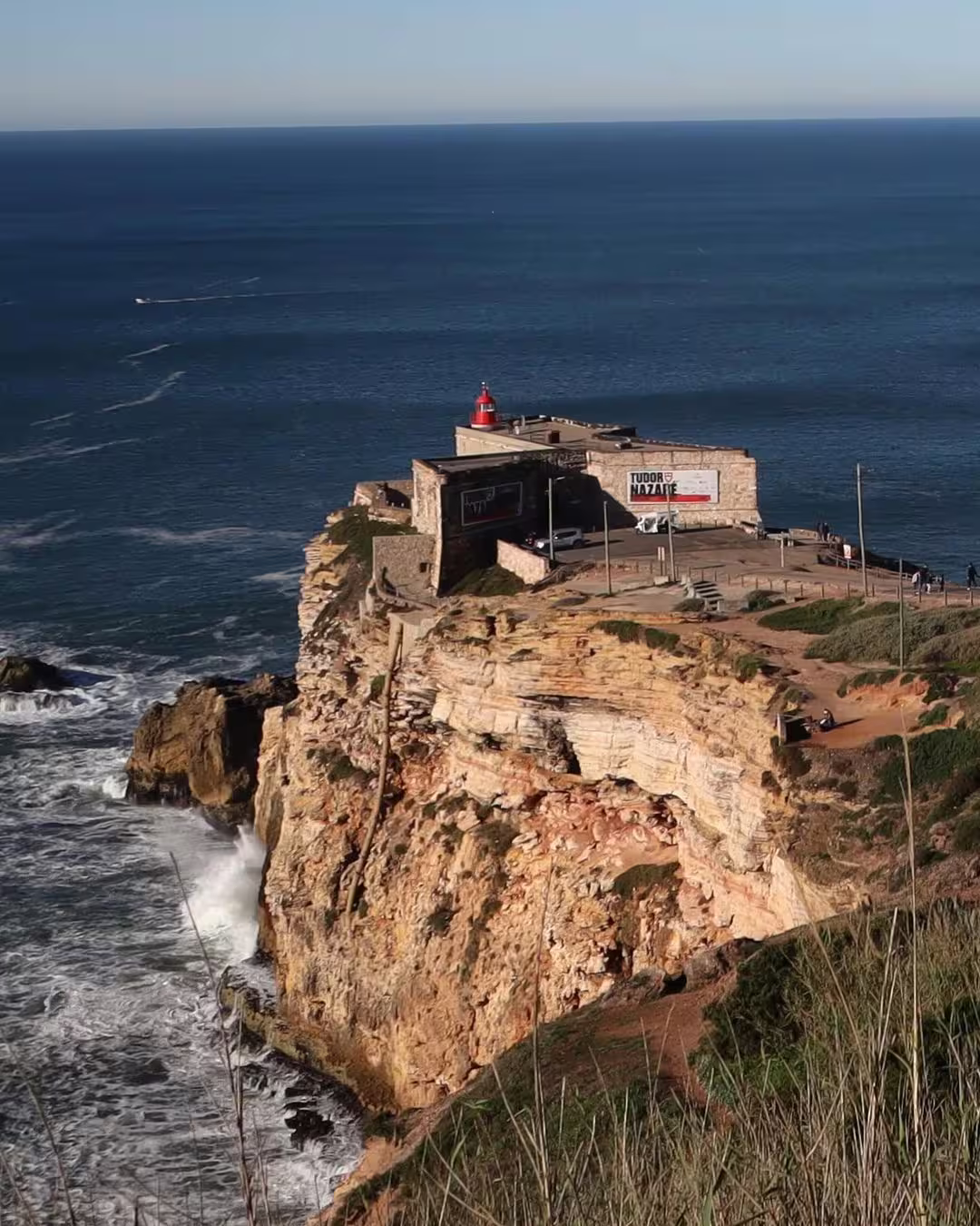 View of Nazaré's iconic cliff-top lighthouse overlooking the Atlantic Ocean, perfect for the Giant Waves Surf Experience.
