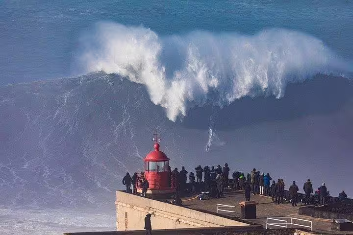Dramatic ocean wave crashing near the iconic Nazaré lighthouse on Portugal's West coast, a must-see on the tour.