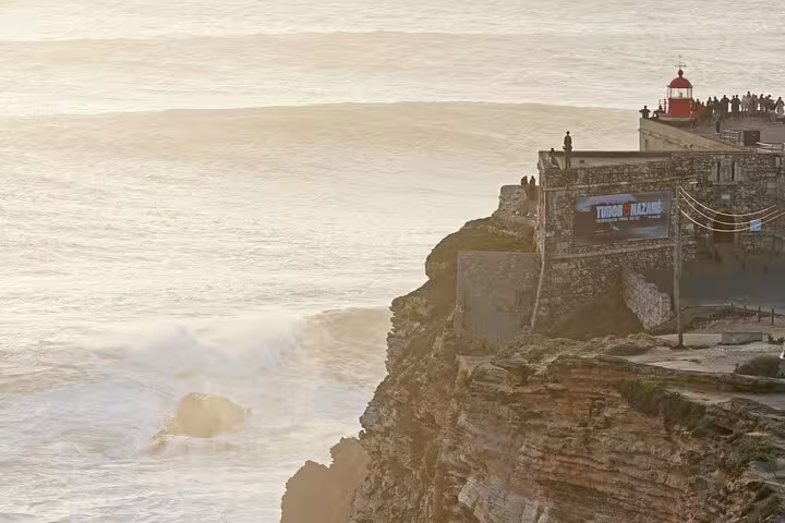 Scenic view of Nazaré's iconic cliffside lighthouse at sunset, a popular stop on the Porto to Lisbon private transfer tour.
