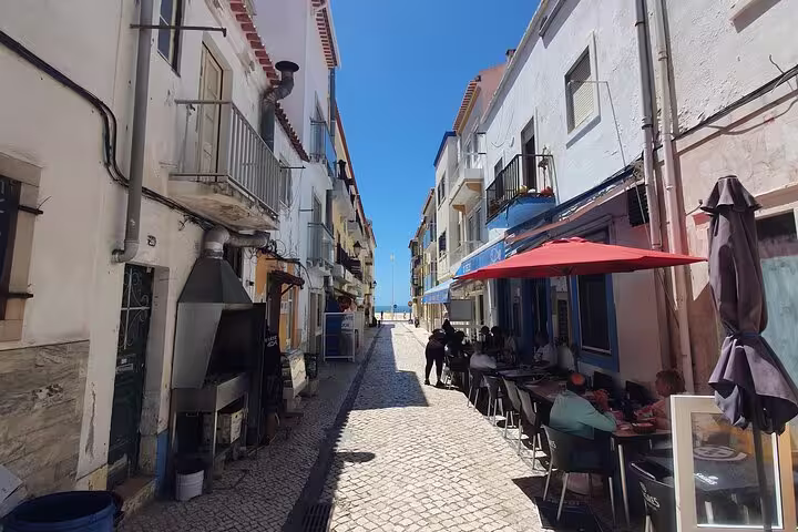 Charming narrow street in Nazaré with outdoor café seating and view of the ocean, part of the Fátima, Nazaré, Batalha & Óbidos tour.