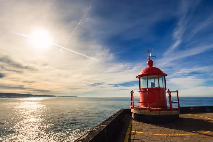 Scenic view of the red lighthouse at Nazaré, Portugal, overlooking the ocean under a bright blue sky.