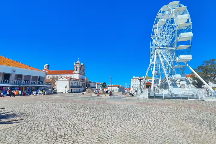 Scenic view of Nazaré's vibrant square featuring a Ferris wheel and historic church, perfect for an unforgettable tour.