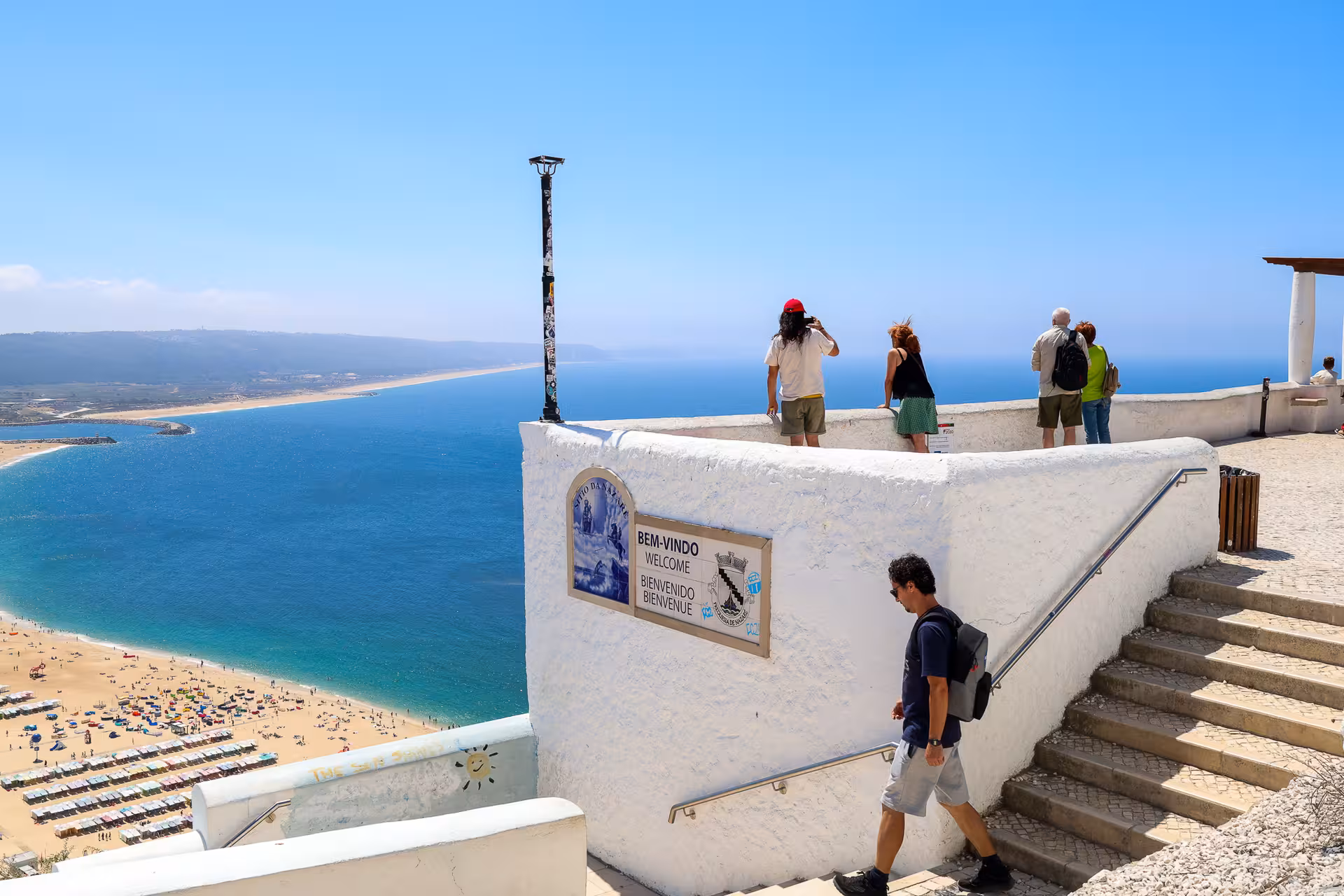 Tourists enjoying panoramic ocean views from Nazaré's scenic viewpoint on a sunny day.