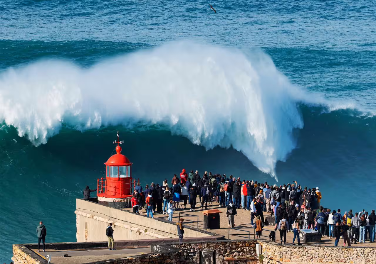 Tourists watch massive waves at Nazaré lighthouse, a highlight on the Fatima and Nazaré tour from Lisbon.