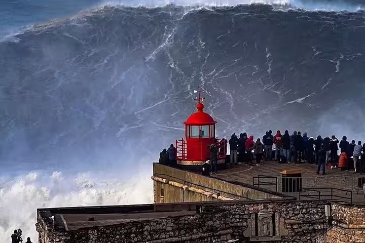 Witness the breathtaking waves at Nazaré's iconic lighthouse, a must-see highlight on the tour from Lisbon.