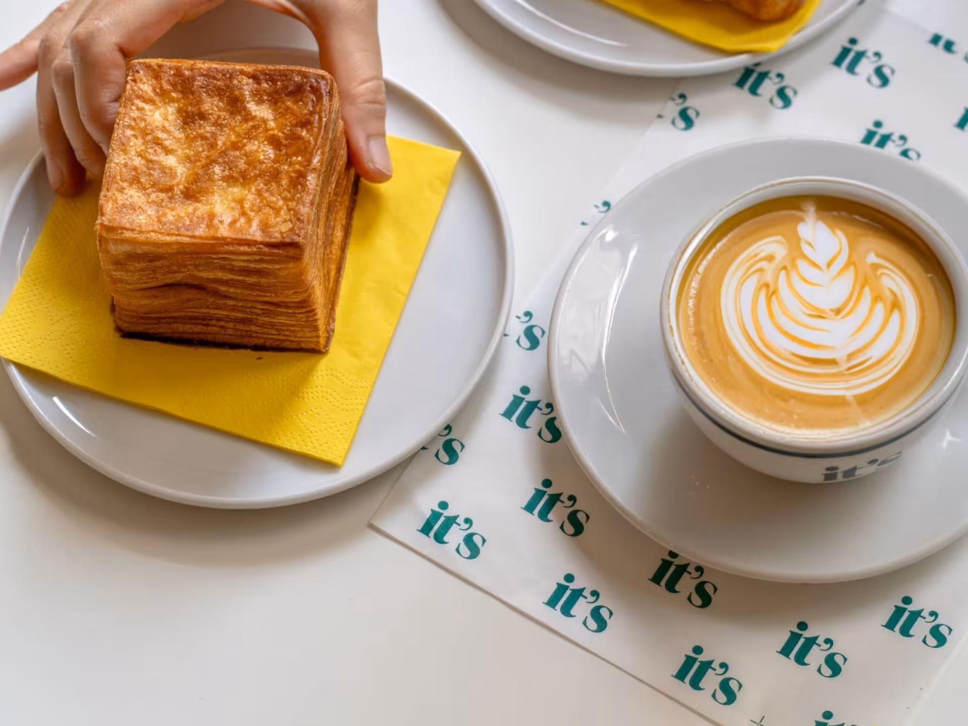 A hand reaching for a layered pastry paired with an intricately designed latte, perfect for a Neapolitan coffee tour.