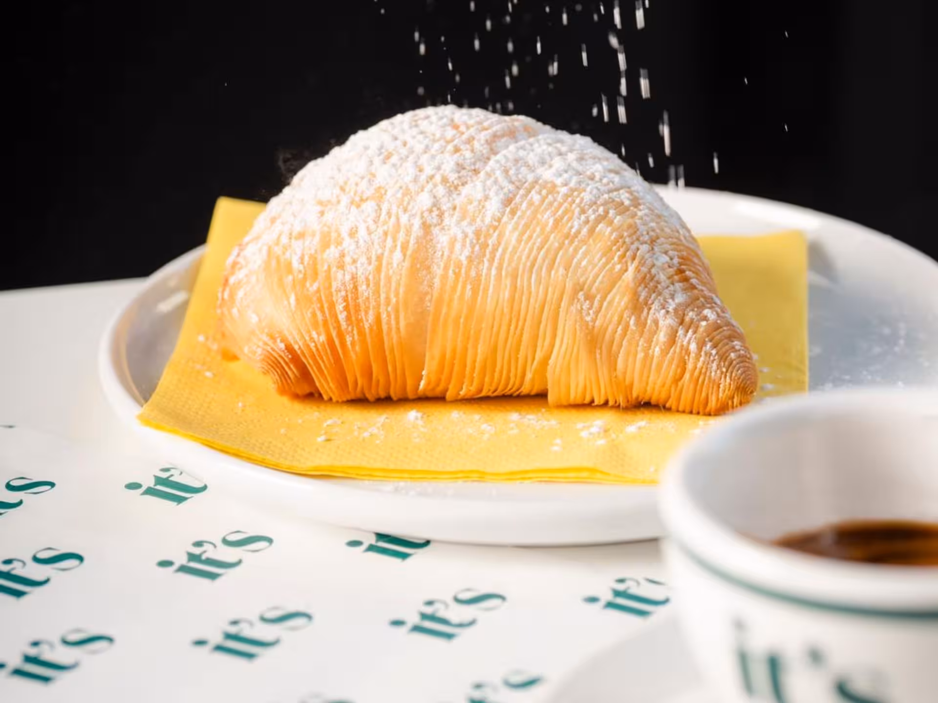 Delicious sfogliatella pastry dusted with powdered sugar, served with Neapolitan coffee on a yellow napkin.
