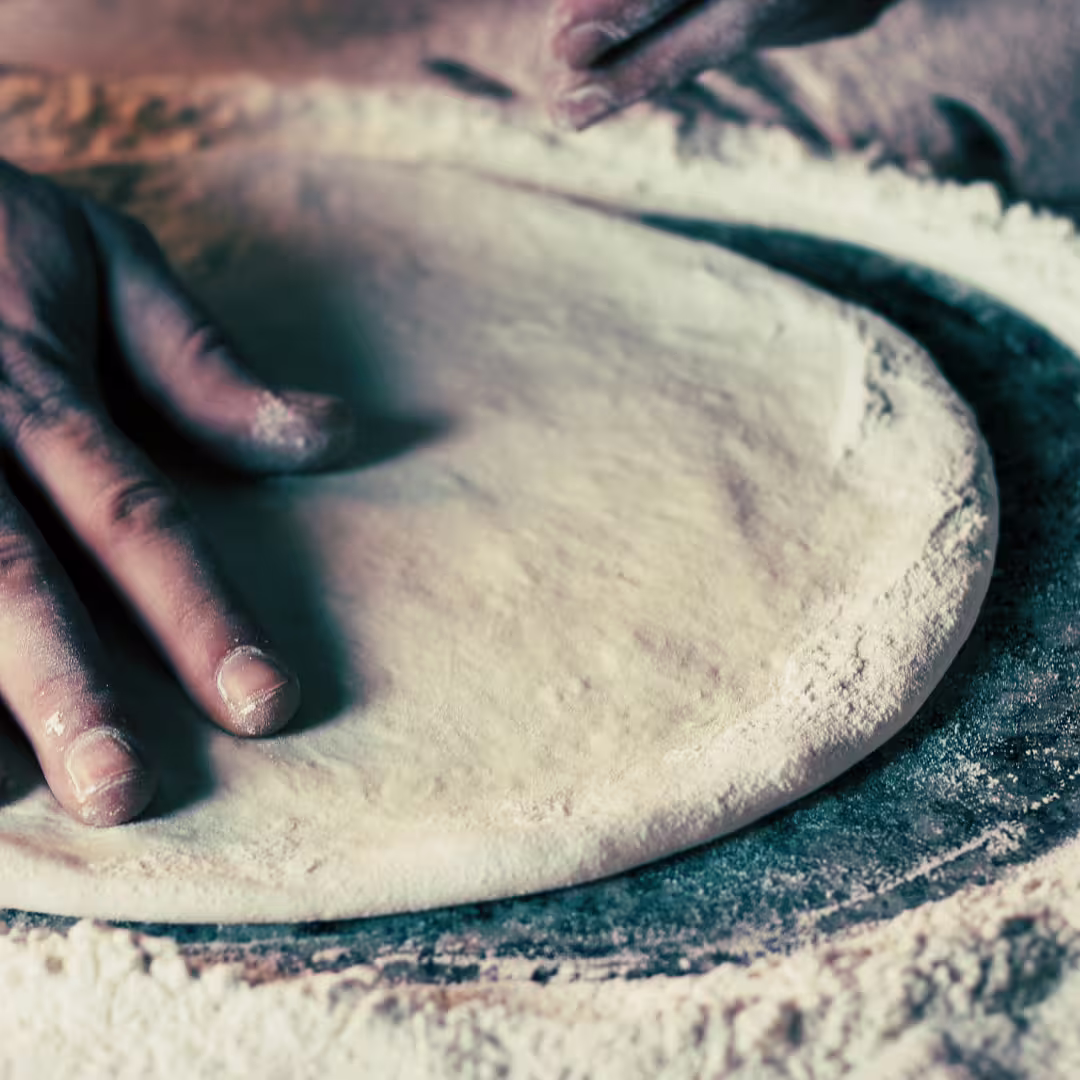 Hands shaping traditional Neapolitan pizza dough on floured counter during hands-on Naples pizza making class