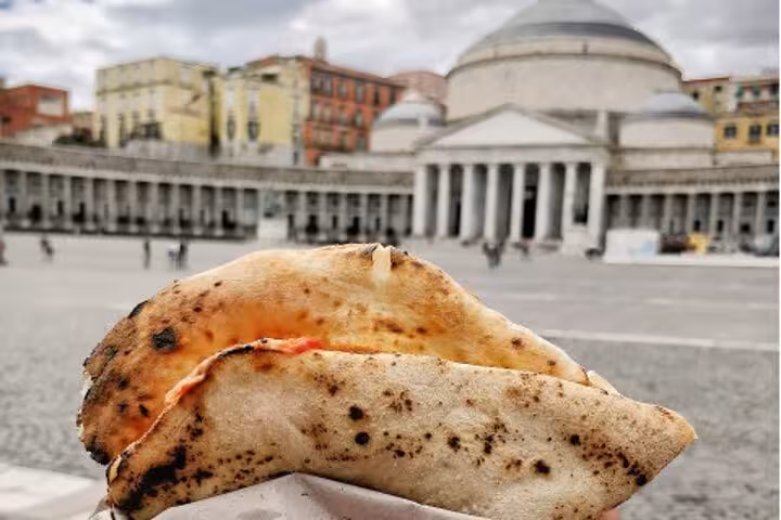 Authentic Neapolitan pizza held in front of Piazza del Plebiscito in Naples.