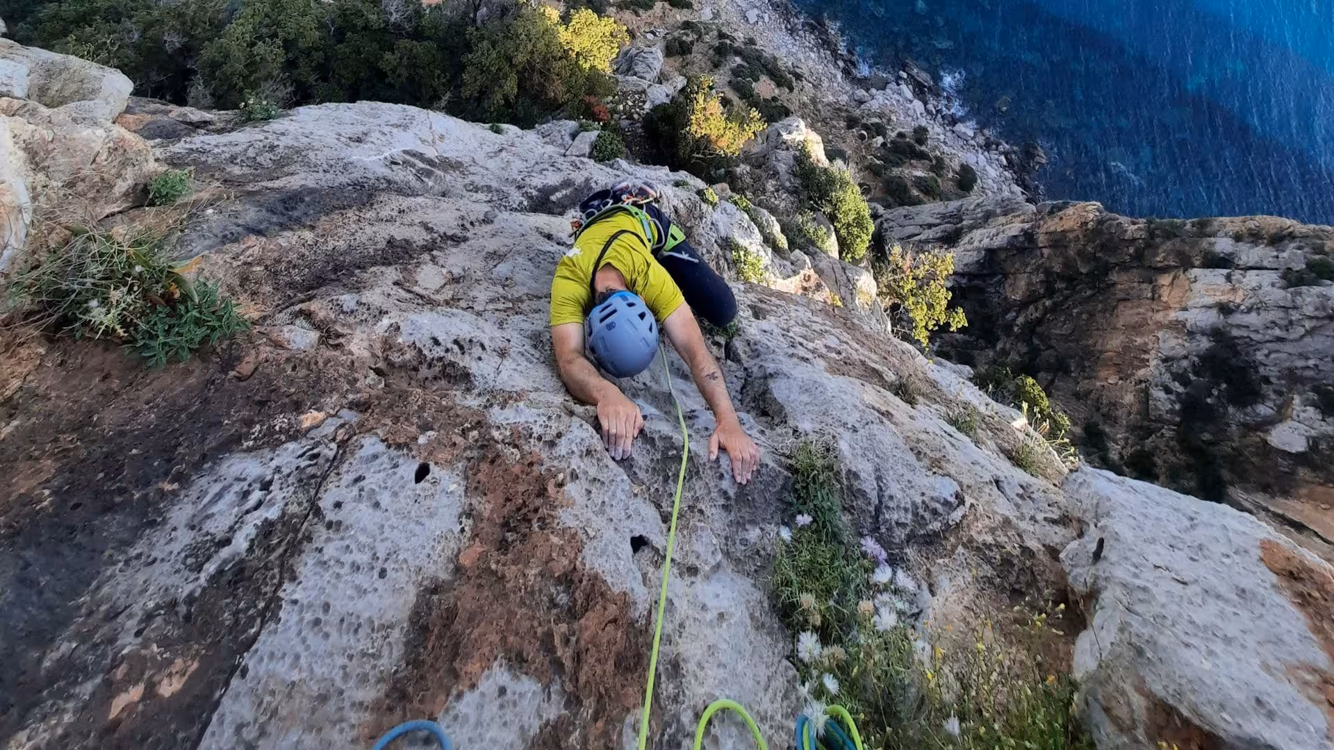 Adventurous climber tackles steep rock face on Masua cliff in Nebida, overlooking shimmering sea.