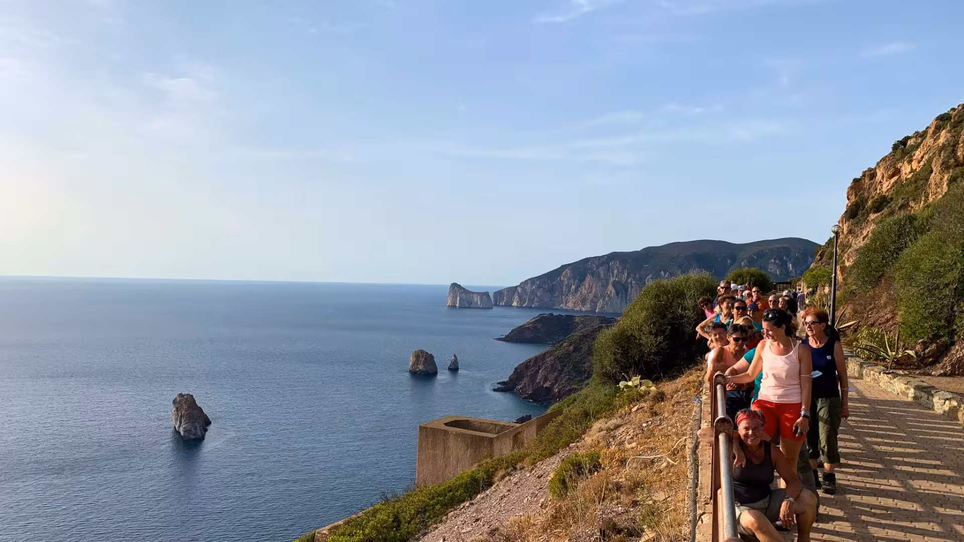 Hikers enjoy scenic coastal views along the Nebida to Masua trail, with dramatic cliffs and azure waters in Iglesias, Sardinia.