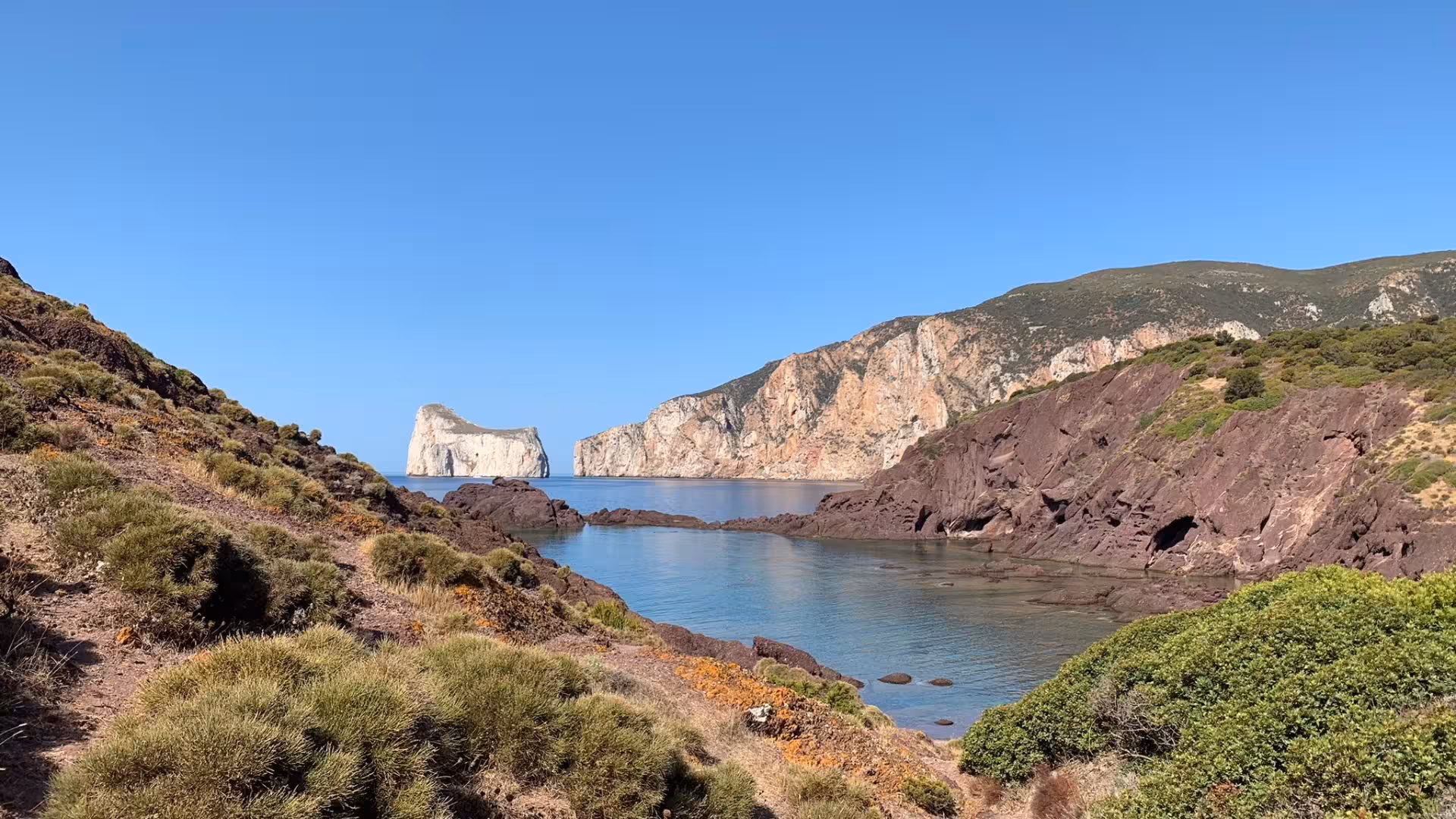 Scenic coastal view from Nebida to Masua hike with lush greenery, rocky cliffs, and clear blue waters, ideal for nature lovers.