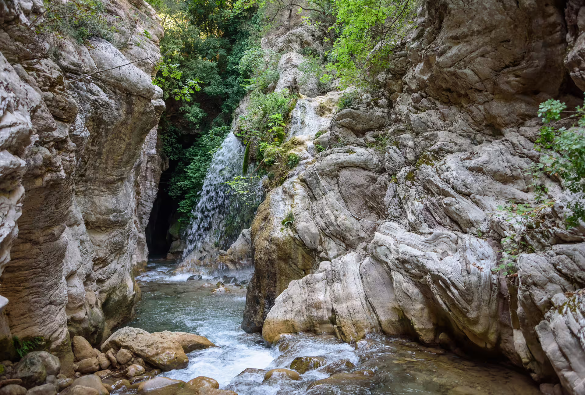 Waterfall in Neda River gorge with clear pools and limestone cliffs, scenic river trekking in Greece