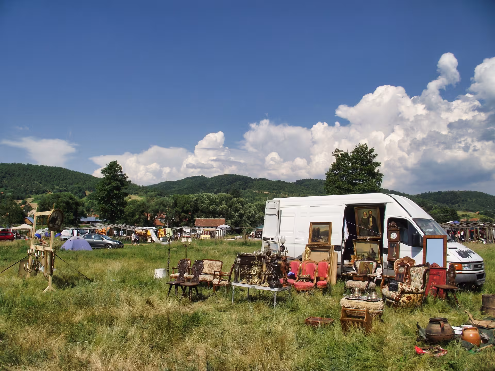 Antique furniture and vintage paintings spread across a green field at the scenic Negreni Flea Market in Romania